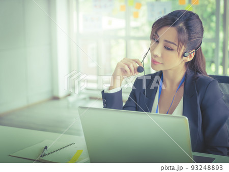 Asian female customer service is answering call on headphone in an operator service office. Asian female customer service is answering call on headphone in an operator service office. 93248893
