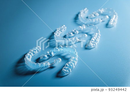 Close up invisible aligners on blue background with copy space. Plastic braces for teeth alignment. Set of three pairs of aligners on a blue background 93249442