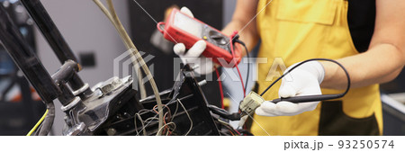 Mechanic using multimeter checks voltage level motorcycle battery motorcycle garage 93250574
