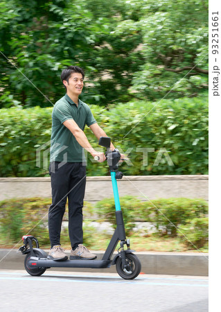 電動キックボードで街を走行する若い男性 93251661
