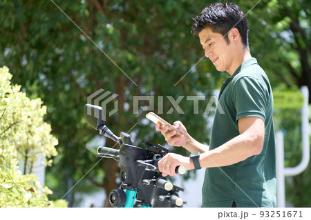 電動キックボードのポートにてスマホの画面を見る若い男性 93251671