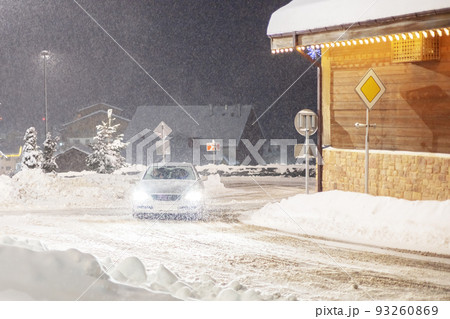 The car is driving down the night street in the snow. Snowfall on the night road. Car driving on a snowy night road The car is driving down the night street in the snow. Snowfall on the night road. Car driving on a snowy night road 93260869