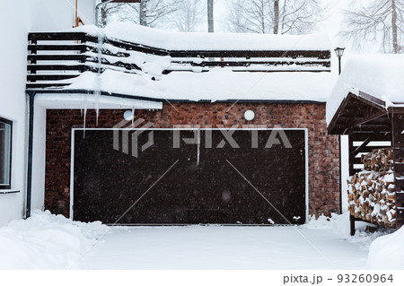 Automatic garage door of a cottage in a snowfall. Winter house with automatic garage doors. Mansion in the winter forest. Winter courtyard of a private cottage Automatic garage door of a cottage in a snowfall. Winter house with automatic garage doors. Mansion in the winter forest. Winter courtyard of a private cottage 93260964