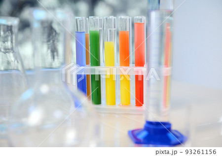 Focus on test tubes with rainbow colored chemicals and reagents standing on tripod. Blurred foreground with graduated cylinder, flasks and measuring glass labware. Chemistry, science concept Focus on test tubes with rainbow colored chemicals and reagents standing on tripod. Blurred foreground with graduated cylinder, flasks and measuring glass labware. Chemistry, science concept 93261156