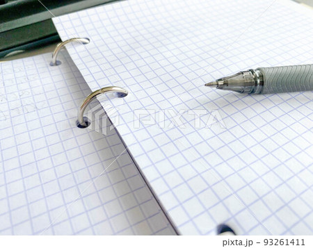 on the table lies a notepad for notes on paper clips in small cells. records for work. on the pages is a pen with a blue rod and a thin lead 93261411