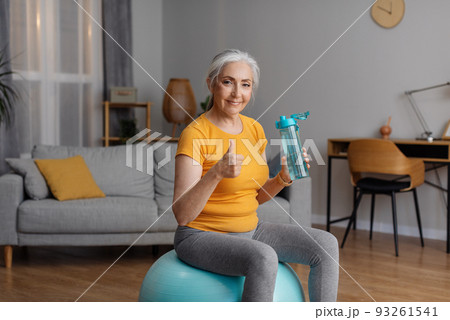 Stay hydrated. Happy senior female holding bottle with fresh water and showing thumb up gesture, sitting on fitball Stay hydrated. Happy senior female holding bottle with fresh water and showing thumb up gesture, sitting on fitball 93261541