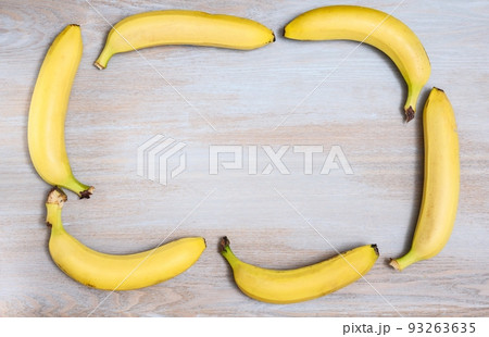 Yellow ripe bananas are laid out as a frame for text on a wooden textured surface - top view. 93263635