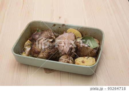 A hot green ceramic dish filled with delicious meat stew with roasted vegetables cooked in a wood fired oven at the farm for a family weekend dinner placed on a table with a textured surface. 93264718