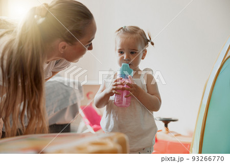 Little girl drinking water from plastic bottle in playing room at home Little girl drinking water from plastic bottle in playing room at home 93266770