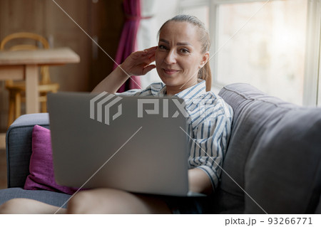 Female freelancer in casual clothes sitting on sofa and using laptop at home looking camera Female freelancer in casual clothes sitting on sofa and using laptop at home looking camera 93266771