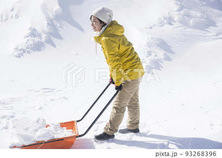 吹雪の中雪かきをする若い女性　除雪イメージ　スノーダンプ 93268396