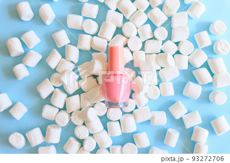 Nail polish small glass bottle flat lay. Unbranded mockup and white little marshmallows a lot on blue background. Professional manicure concept, top front view. 93272706