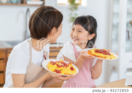 キッチンで出来上がったオムライスを手に微笑む小学生の女の子とママ キッチンで出来上がったオムライスを手に微笑む小学生の女の子とママ 93272850
