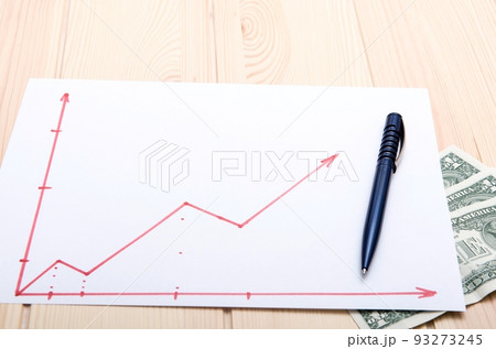 A sheet of paper depicting a drawing of a graph of rising stock prices depicting a stock market for securities with dollars under the paper A sheet of paper depicting a drawing of a graph of rising stock prices depicting a stock market for securities with dollars under the paper 93273245