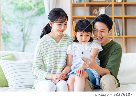 リビングでスマホを見る若い家族 93276107