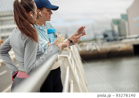 Two young sporty woman standing on bridge and have a rest after morning running in city Two young sporty woman standing on bridge and have a rest after morning running in city 93276140