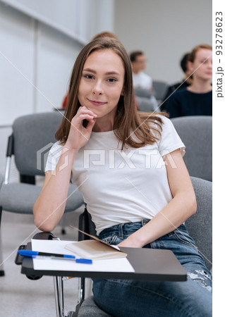 Portrait of a young pretty girl student during college classes, she is sitting in the audience among other student 93278623