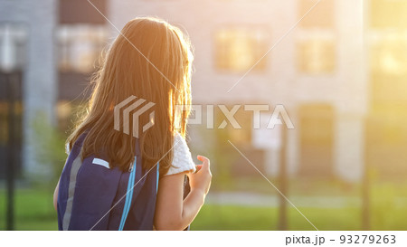 Girl goes to school looking at illuminated windows at sunset Girl goes to school looking at illuminated windows at sunset 93279263