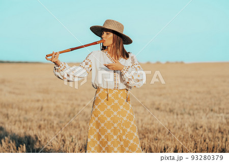 Woman playing on woodwind wooden flute - ukrainian telenka or tylynka in wheat field. Folk music Woman playing on woodwind wooden flute - ukrainian telenka or tylynka in wheat field. Folk music 93280379