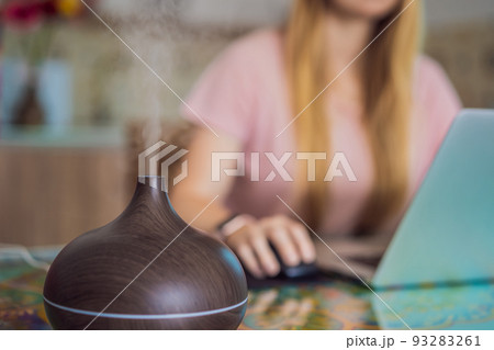 Essential oil diffuser on the table steaming while woman using laptop Essential oil diffuser on the table steaming while woman using laptop 93283261