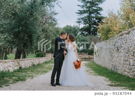 Happy stylish smiling couple walking in Tuscany, Italy on their wedding day. The bride and groom walk down the street by the hands. A stylish young couple walks. Husband and wife communicate nicely Happy stylish smiling couple walking in Tuscany, Italy on their wedding day. The bride and groom walk down the street by the hands. A stylish young couple walks. Husband and wife communicate nicely 93287044