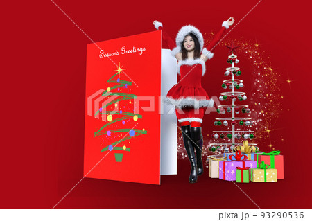 クリスマスのコスチュームを着てグリーティングカードとプレゼントの箱とツリーの間に両手を広げて立つ女性 93290536
