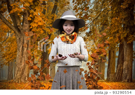 紅葉した森林を背景に観光地でどんぐりと松ぼっくりを拾って感動する女性旅行者 93290554