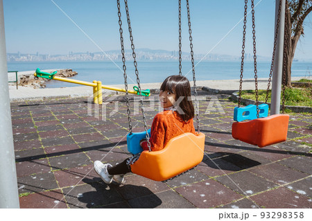 little girl playing in empty playground next to the sea little girl playing in empty playground next to the sea 93298358