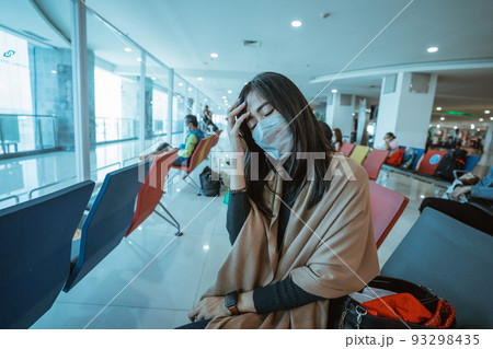 unwell young woman wearing mask sitting on airport terminal 93298435