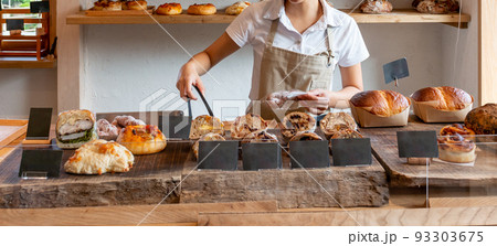 パン屋　ベーカリーショップ　トングで焼きたてパンを掴むエプロン姿の女性店員	 93303675