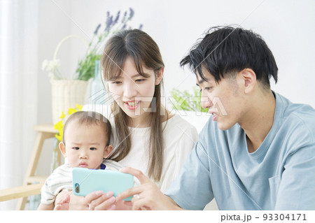 リビングでスマホを見る両親と赤ちゃん リビングでスマホを見る両親と赤ちゃん 93304171