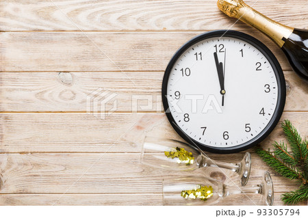 New year celebration concept with a bottle of champagne and two glasses toasting. Christmas gift box, alarm clock and fir tree branch on colored table. Top view Copy space New year celebration concept with a bottle of champagne and two glasses toasting. Christmas gift box, alarm clock and fir tree branch on colored table. Top view Copy space 93305794