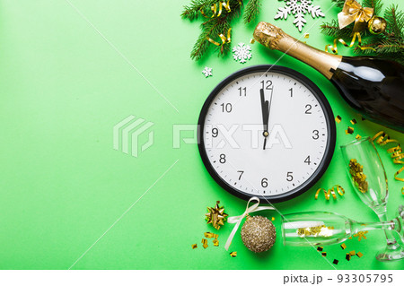 New year celebration concept with a bottle of champagne and two glasses toasting. Christmas gift box, alarm clock and fir tree branch on colored table. Top view Copy space New year celebration concept with a bottle of champagne and two glasses toasting. Christmas gift box, alarm clock and fir tree branch on colored table. Top view Copy space 93305795