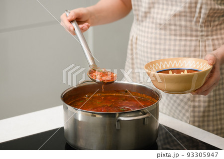 A woman pours freshly prepared Ukrainian borscht onto a plate. 93305947