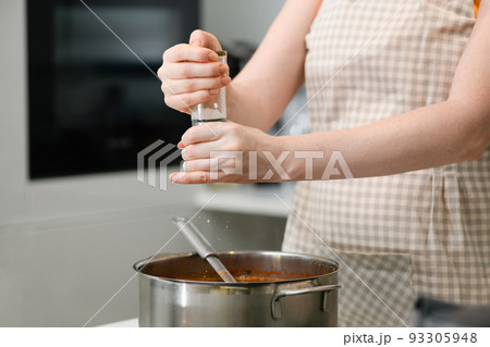 A woman in an apron adds spices to borscht. 93305948
