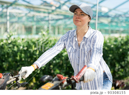 Young woman operating a cultivator in a greenhouse on sunny day 93308155