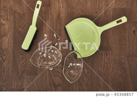 A close-up view from above of a split transparent cup with soup and brushes with a dustpan for cleaning. The concept of home cleaning in the apartment. High quality photo 93308857