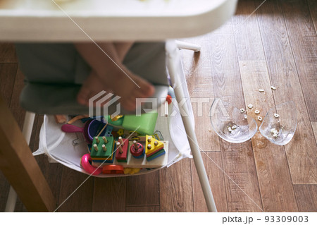 A broken transparent plate is visible in the background. In the foreground - children's legs in a high chair. The concept of kitchen accidents is dangerous for young children. High quality photo 93309003