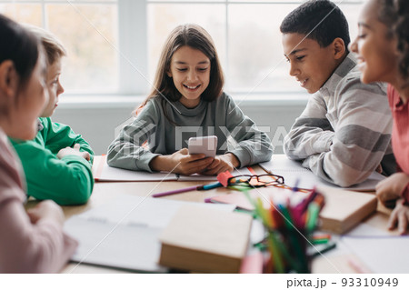 Cheerful Diverse School Children Using Cellphone Sitting In Modern Classroom 93310949