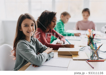 Happy Schoolgirl Sitting At Desk Smiling To Camera In Classroom Happy Schoolgirl Sitting At Desk Smiling To Camera In Classroom 93311136