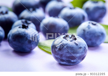 Close-up of a blueberry with green leaves and water drops on a purple background 93312205