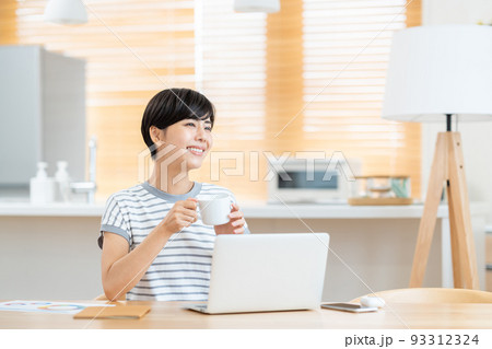 リビングでテレワーク中に休憩する女性 リビングでテレワーク中に休憩する女性 93312324