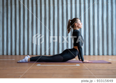 Woman in cobra pose, she exercising on floor her arms extended and upper body raised upward back hyperextended. Woman in cobra pose, she exercising on floor her arms extended and upper body raised upward back hyperextended. 93315649