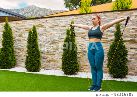 young sportswoman, stretching her body muscles with elastic bands outdoors in the garden of her house. concept of health and well-being. young sportswoman, stretching her body muscles with elastic bands outdoors in the garden of her house. concept of health and well-being. 93316385