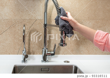Home cleaning in the kitchen. Girl wipes the faucet with a rag Home cleaning in the kitchen. Girl wipes the faucet with a rag 93316511