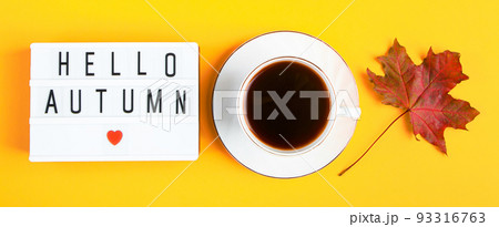 Hello autumn concept. Cup of coffee and sign with inscription on yellow background. Fallen leaves and hot drink. 93316763