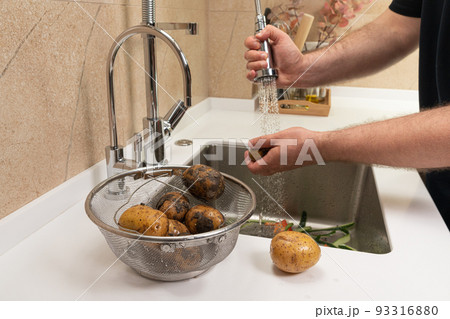 Man washing potatoes for lunch in a modern kitchen Man washing potatoes for lunch in a modern kitchen 93316880
