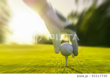 Closeup of golfer wearing glove placing golf ball on a tee at golf course with motion blur effect 93317740