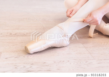 A seated ballerina tightens her pointe shoes A seated ballerina tightens her pointe shoes 93318203