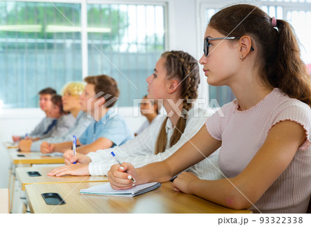 Teenagers listening to lecturer and writing in notebooks in classroom 93322338